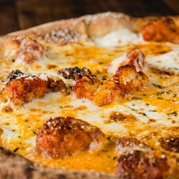 Close-up of a pizza with a golden crust, melted cheese, and crispy orange chicken pieces.