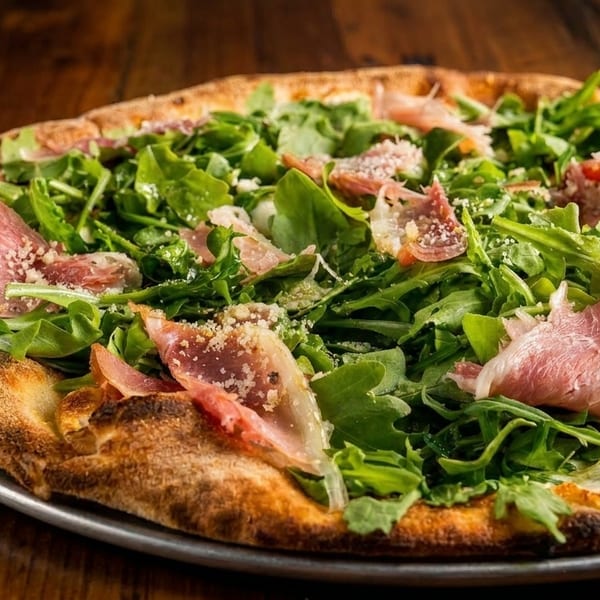 A whole pizza topped with fresh arugula, prosciutto, and grated cheese on a metal pan.