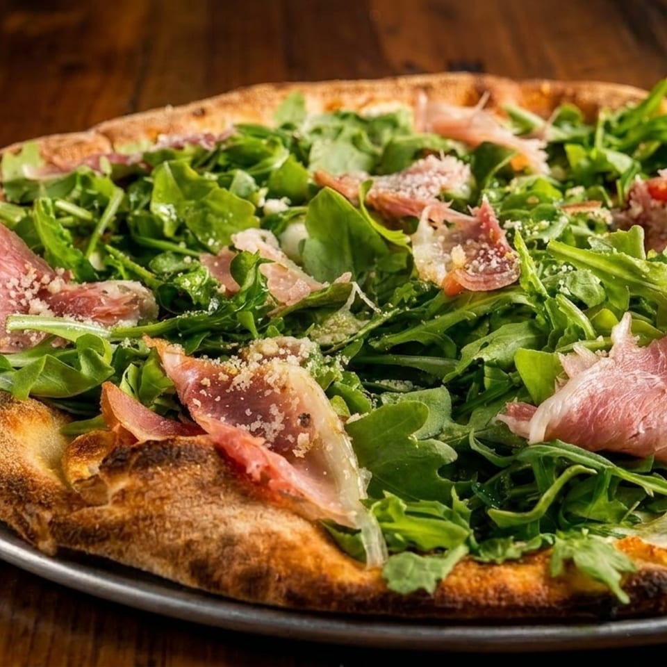 A whole pizza topped with fresh arugula, prosciutto, and grated cheese on a metal pan.